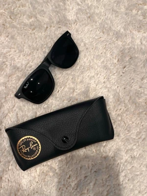 Svarta RayBan  solglasögon - Klassiska svarta Ray-Ban Wayfarer solglasögon med ikonisk form och Ray-Ban-logga på bågen. Snygg och tidlös design som passar till allt. Kommer med original svart fodral i skinnimitation.