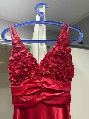 Röd långklänning i satin - Säljer en elegant röd långklänning med slät och glansig finish. Klänningen har en klassisk och enkel design utan mönster, perfekt för dig som gillar stilrena plagg. Materialet är satin som ger en lyxig känsla och vacker lyster.