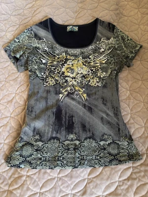 Grå/grön mönstrad t-shirt - Snygg vintage grå t-shirt med korta ärmar och unikt blommigt mönster i vitt, grönt och gult framtill. T-shirten har rund halsringning och dekorativa detaljer längs nederkanten och axlarna. 100% cotton. PRIS KAN DISKUTERAS🤍