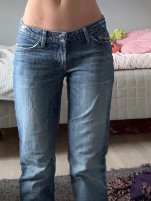 Jeans - Säljer ett par klassiska blå jeans från Replay med rak passform och låg midja. Jeansen har slitningar på bakfickan och snygga detaljer vid fickorna. Tillverkade i denim med en autentisk tvättad look och femficksmodell.