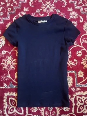 Mörkblå t-shirt från Bershka - En enkel och stilren mörkblå t-shirt från Bershka. Modellen är klassisk med rund halsringning och korta ärmar. Perfekt basplagg i garderoben och lätt att matcha med olika outfits. Har små fläckar som ses på sista bilden som var där när jag köpte den. Annars helt ny och endast testad.