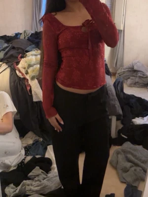 Röd långärmad topp med rosett - Trendig röd långärmad topp med subtilt blommönster och söt rosettdetalj vid urringningen. Figurnära passform och något croppad längd. Perfekt för dig som vill ha en feminin och stilren look.