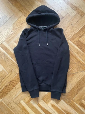 Svart hoodie från Superdry - Svart hoodie från Superdry med broderad logga på bröstet. Bra skick. Matchar till de mesta.
