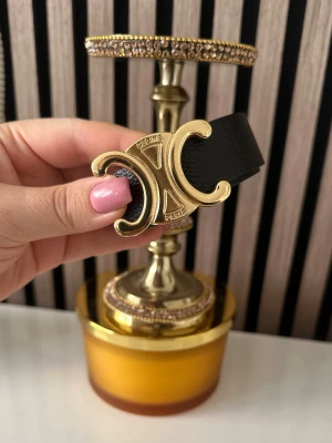 Svart skärp med guldspänne  -  Skärpet är tillverkat i skinn och har en elegant och tidlös design som lyfter vilken outfit som helst.