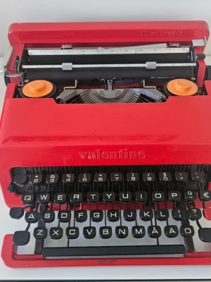 Röd skrivmaskin Olivetti Valentine - Säljer en ikonisk röd skrivmaskin av modellen Valentine från Olivetti. Maskinen har ett retro utseende med svarta tangenter och orange detaljer. Perfekt för dig som gillar vintageprylar och snygg design. Inte testad och används som decor.hemma!