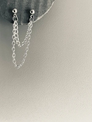 By prisförslag- 1 st Silvrigt dubbel örhänge med dubbla kedjor - Snyggt silvrigt örhänge med två tunna kedjor som hänger mellan två små kulor. Minimalistisk och modern design, perfekt för dig som gillar stilrena accessoarer. Materialet ser ut att vara metall i silverfärg.