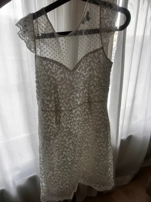 Student klänning - vit spets klänning - Söt vit klänning i spets med transparenta partier upptill och volangärmar. Klänningen har ett vackert spetsmönster över hela och en lätt figurnära passform. Perfekt för dig som gillar romantisk och feminin stil.