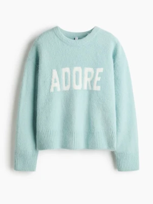 Ljusblå stickad tröja med text - Mysig ljusblå stickad tröja med vit text 'ADORE' framtill. Tröjan har rund halsringning, långa ärmar och ribbstickade muddar vid ärmslut och nederkant. Materialet är fluffigt och ger en soft känsla.