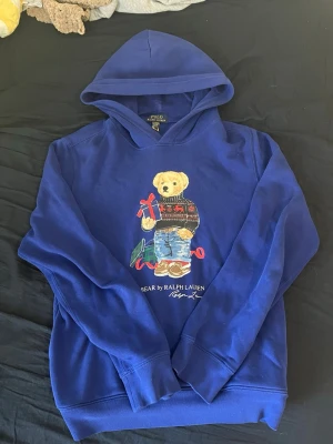 Blå hoodie Polo Bear Ralph Lauren - Blå hoodie från Ralph Lauren med den ikoniska Polo Bear-trycket på bröstet. Hoodien har huva och långa ärmar, samt ribbade muddar. Materialet känns mjukt och skönt, perfekt för en chill och avslappnad stil. Storlek 170. Tar emot  erbjudanden 🙂