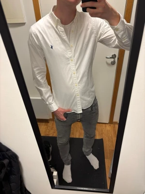 Vit skjorta från Polo Ralph Lauren - Klassisk vit skjorta från Polo Ralph Lauren i slim fit med button-down krage och broderad logga på bröstet. Tillverkad i tunn bomullstwill som känns lätt och fräsch. Perfekt för dig som gillar stilrena och tidlösa plagg.