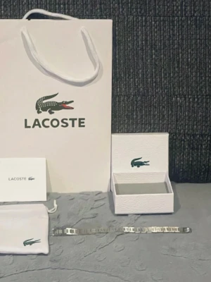 Lacoste silverfärgad armband - Säljer en stilren klocka från Lacoste med silverfärgat armband i metall. Klockan kommer med originalförpackning, påse och manual. Perfekt för dig som gillar klassiska accessoarer med en modern touch och ikonisk krokodillogo.