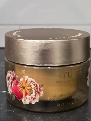 Rituals Intuita whipped body cream - Rituals Intuita whipped body cream med sandelträ och vaniljessens. Kommer i en rund, transparent burk med metallfärgat lock och blommigt motiv. Perfekt för dig som vill ha en lyxig och väldoftande kroppskräm.