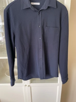 Mörkblå skjorta från Zara - Stilren mörkblå overshirt skjorta från Zara med klassisk krage, bröstficka och knappar framtill. Perfekt för dig som gillar enkel och clean stil, passar bra att ha över en T-shirt. Ny pris: 399kr, mitt pris: 199kr