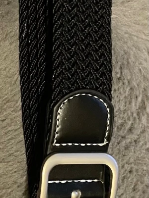 Svart flätat bälte med skinn-detaljer - Snyggt svart bälte med flätad design och detaljer i svart skinn med vit söm. Spännet är i silverfärgad metall och bältet har en stilren look som passar till många outfits.obs går att upphämtas i södra Stockholm 