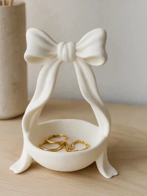 Smyckesskål med rosett  - smyckesskål i vit med en stor dekorativ rosett upptill. Perfekt för att förvara ringar, örhängen eller andra småsmycken. Skålen har en söt och trendig design som passar perfekt på sminkbordet eller nattduksbordet.