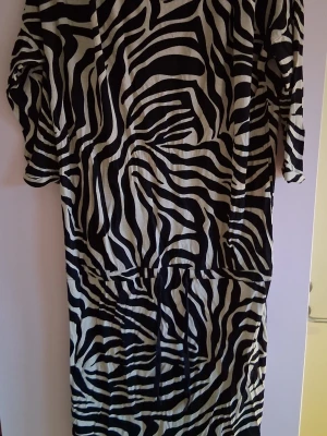 Zebramönstrad långklänning - Cool långklänning med svartvitt zebramönster och trekvartsärm. Klänningen har en lös passform och är perfekt för dig som vill sticka ut med ett djuriskt print. Tillverkad i ett mjukt och bekvämt material.