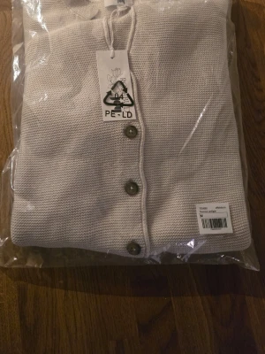 Beige stickad kofta med knappar - En ljusbeige stickad kofta med knappar i hornimitation fram. Denna snygga cardigan har ståkrage och dekorfickor. Dessa fina koftor är perfekta när det blir lite svalt på sommarkvällarna. OBS! Koftan är nätt i storleken. Nypris: 799,00 SEK  https://joyshop.se/products/francine-cardigan-3?srsltid=AfmBOopAubzT0C1DT5LtKFucTDJgI5chXdXhjHYIcFklI6Wja_oBgT9O