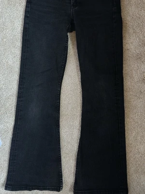 Svarta bootcut jeans från Gina Tricot  - Säljer ett par svarta bootcut jeans från Gina Tricot med klassisk femficksdesign och broderade bakfickor. Jeansen har en något utsvängd passform nertill och är tillverkade i denim. Perfekta för en avslappnad och trendig look.