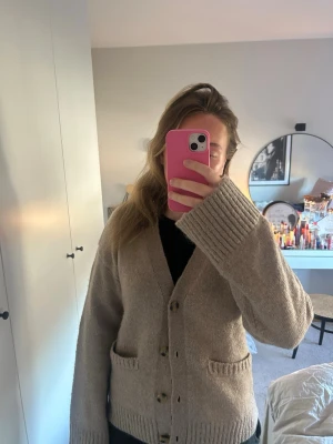 Beige stickad kofta med knappar - Mysig beige stickad kofta med v-ringning och stora knappar framtill. Aldrig använd 