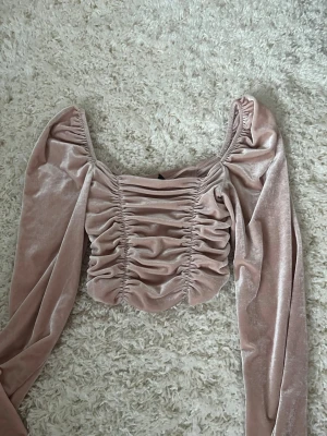 Ljusrosa sammetsblus med puffärm - Supersöt ljusrosa blus i mjuk sammet med långa puffärmar och snygg rynkning framtill. Croppad modell med fyrkantig ringning som ger en trendig vibe. Perfekt för dig som vill sticka ut lite extra!