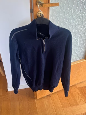 Mörkblå Kashmirziptröja från ZegnaSport - Mörkblå stickad tröja från ZegnaSport med halv dragkedja framtill och hög krage. Tröjan har långa ärmar, ribbade muddar och en diskret kontrastdetalj på axeln. Perfekt för dig som gillar stilren och sportig design. Nypris 4990kr