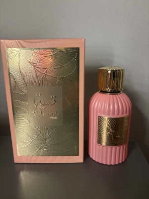 Qissa Pink parfym i rosa flaska - Qissa Pink parfym i en snygg rosa flaska med gulddetaljer och räfflad design. Flaskan har en lyxig känsla med ett guldfärgat lock och matchande etikett. Kommer i en elegant ask med bladmönster i guld och rosa. Perfekt för dig som gillar stilrena och trendiga dofter.