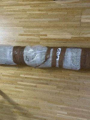 Beige och vit randig matta - Säljer en rullad matta i beige och vitt med randigt mönster. Mattan är inslagen i plast och tejp för enkel transport. Perfekt för att ge rummet en mysig känsla och passar bra på trägolv.