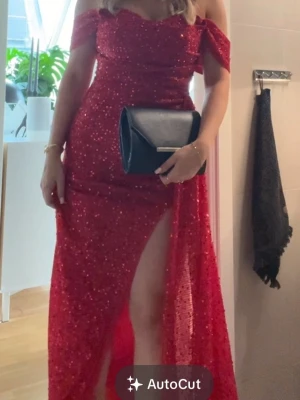 Röd balklänning med slits - Säljer en röd balklänning täckt av glittriga paljetter. Klänningen har korta ärmar, figurnära passform och en hög slits framtill som ger en snygg och dramatisk look. Perfekt för bal eller fest där du vill sticka ut.