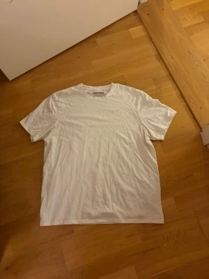 Vit t-shirt från Nike i bomull - Klassisk vit t-shirt från Nike med broderad logga på bröstet. T-shirten har rund halsringning och är tillverkad i mjuk bomull. Perfekt basplagg med enkel och stilren design.