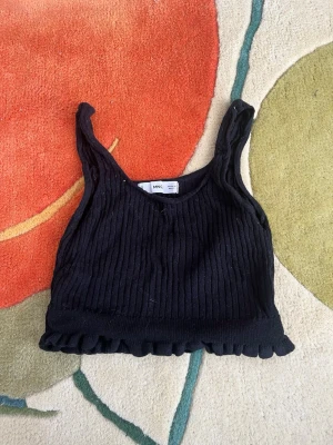 Svart ribbad linnetopp från mango  - Ett svart cropped linne från Mango med volangkant. Perfekt för layering. .