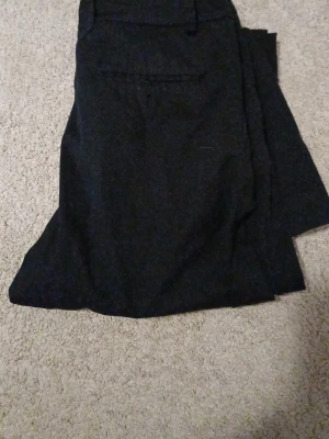 Svarta kostymbyxor med fler i passform - Snygga svarta kostymbyxor med klassisk fler i passform och diskreta fickor bak. Perfekta för en stilren look. Materialet ser ut att vara en mjukare vävd textil som ger en dressad känsla.