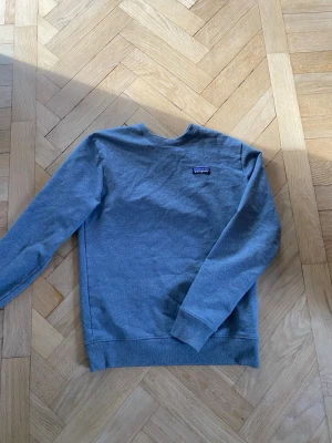 Grå sweatshirt från Patagonia - Snygg grå sweatshirt från Patagonia med klassisk logga på bröstet. Tröjan har rund halsringning, långa ärmar och ribbade muddar. Perfekt för en avslappnad och stilren look. Mjuk bomullsblandning som känns skön mot huden.