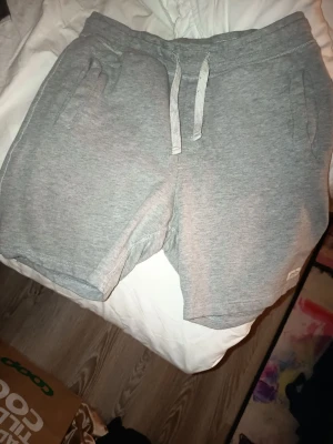 Grå mjukisshorts med snörning - Gråa mjukisshorts med snörning i midjan och fickor på sidorna. Perfekta för en avslappnad stil och tillverkade i mjukt bomullsmaterial. Klassisk passform och enkel design som funkar till det mesta.