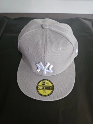 Grå New Era 59FIFTY NY keps - Snygg grå keps från New Era med New York Yankees-logga broderad i vitt framtill. Modellen är 59FIFTY med platt skärm och klassisk passform. Materialet är slitstark bomull och kepsen har broderade ventilationshål samt New Era-logga på sidan.
