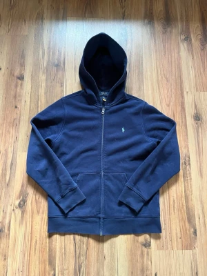 Mörkblå zip hoodie Polo Ralph Lauren - Mörkblå fet polo raffe hoodie med 67 tryck på baksidan. Tröjan mäter 60 cm i längden axel till mudd och 44 cm bröstbredd. 9/10 skick & äkta. 