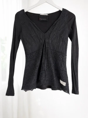 Svart spetsblus från Odd Molly - Svart långärmad blus från Odd Molly med v-ringning och fina spetsdetaljer framtill. Blusen har en feminin passform och dekorativt mönster i tyget. Perfekt att styla med jeans eller kjol för en trendig look.
