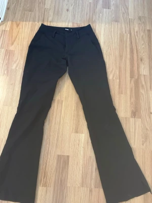Svarta bootcut kostymbyxor - Säljer ett par svarta kostymbyxor med bootcut passform och pressveck. Flärpen man drar upp dragkedjan med har gått av på mitten men den fungerar ändå