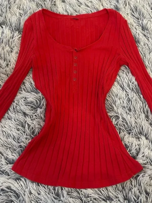 Röd ribbad långärmad topp - Snygg röd ribbad topp med lång ärm och knappar framtill. Figurnära passform och rundad halsringning. 