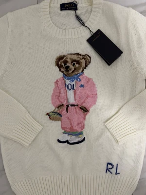 Stickad tröja med en björn  - Osäker på storlek men det är barn storlek. Midjemått 45cm, Längd 58cm, Ärmlängd 59cm