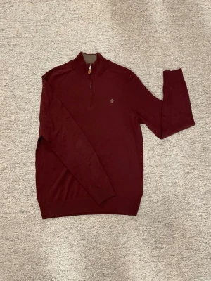 Vinröd zip-tröja från Morris - Vinröd tröja från Morris med halvzip och liten broderad logga på bröstet. Tröjan har ribbade muddar och krage med kontrastfärg på insidan. Materialet är mjukt och stickat, perfekt för lager-på-lager. Snygg och stilren design.