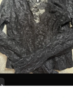 Svart spetsblus från Amisu - Snygg svart långärmad blus från Amisu i genombruten spets med blommigt mönster. Perfekt att styla lager på lager eller med ett linne under. Blusen har v-ringning och är figurnära i modellen.