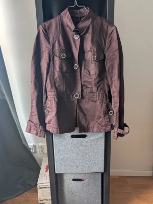 Brun jacka med stora knappar Escada - Snygg brun jacka med markerad midja och stora dekorativa knappar framtill. Jackan har två bröstfickor med lock och långa ärmar med knappar vid ärmslut. Perfekt för dig som vill ha en stilren och trendig look.