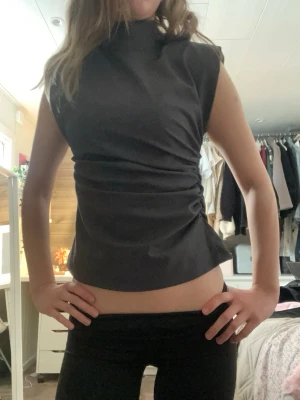 Zara topp - Snygg polotopp med hög hals och ärmlös design. Toppen har en figurnära passform och lätt rynkade detaljer i sidan som ger en cool siluett. Perfekt att styla med jeans eller kjol för en trendig look.