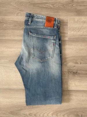 Blå jeans från Replay - Snygga blå jeans från Replay med klassisk femficksdesign och läderpatch bak i midjan. Jeansen är i mycket bra skick. Modell Anbass. Storlek 32/32! Hör av dig 🤙 
