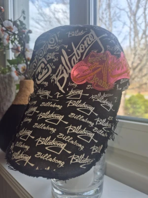 Ny Svart tuff keps från Billabong med tryck! One size - Svart keps från Billabong med vitt all-over-logotryck och en stor rosa broderad detalj på sidan. Kepsen har böjd skärm och råa kanter för en avslappnad streetstil. Perfekt accessoar för dig som gillar skate eller surf vibes. Reglerbar storlek. Helt ny så självklart i toppskick. Endast lappar borttagna. Djur och rökfritt hem 
