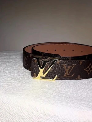 L-V bälte - Stilrent mönstrat bälte – helt nytt  Säljer ett snyggt bälte i klassiskt mönster med guldfärgat spänne. Bältet är helt nytt och oanvänt, i perfekt skick.  Den stilrena designen gör att det passar både till vardag och mer uppklädda outfits – en riktig statement-detalj.