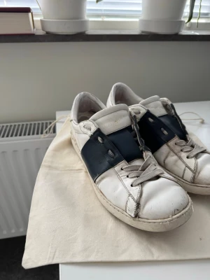Valentino vita sneakers med blå detalj - Snygga vita sneakers från Valentino med en bred mörkblå läderdetalj över sidan.