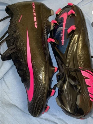 Nike Mercurial svart/rosa fotbollsskor - Säljer ett par Nike Mercurial fotbollsskor i svart med stora rosa detaljer och Nike-logga. Skorna har snörning och är tillverkade i ett lätt syntetmaterial som ger bra grepp på planen. Perfekta för dig som vill sticka ut på fotbollsplanen. Använt dessa 2 gånger men blev lite för stora för mig. Storlek 40,5 men lite större. Passar bra för 41