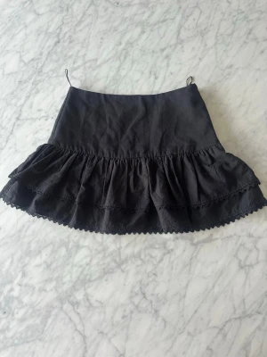 Svart volangkjol från Zara - Supersnygg svart kortkjol från Zara med dubbla volanger och spetsdetaljer längst ner. Kjolen är tillverkad i mjukt bomullstyg. Den är använd tre gånger.