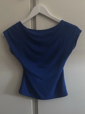 Blå topp med öppen rygg - Snygg blå topp med bred halsringning och öppen rygg. Modellen är ärmlös och har en figurnära passform som framhäver siluetten. Perfekt för dig som vill ha en enkel men ändå trendig look.